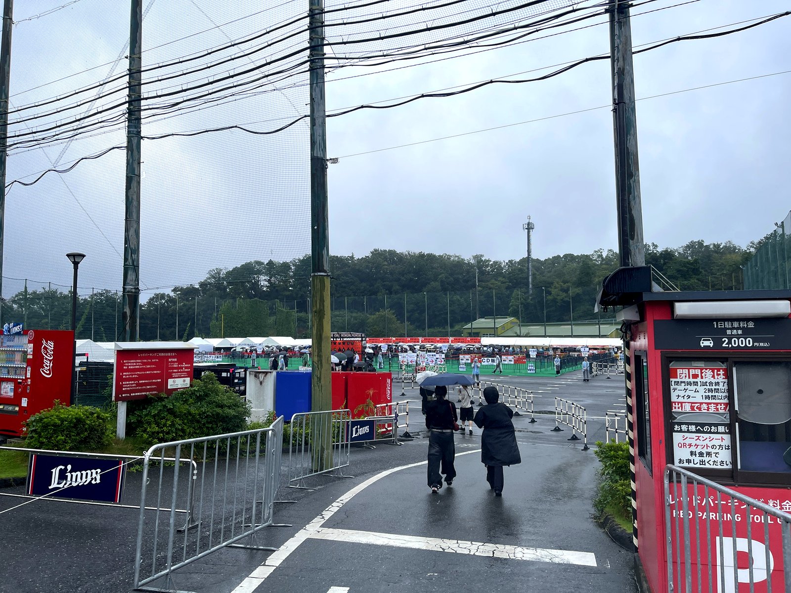 雨のレッドパーキング入口と傘をさす来場者