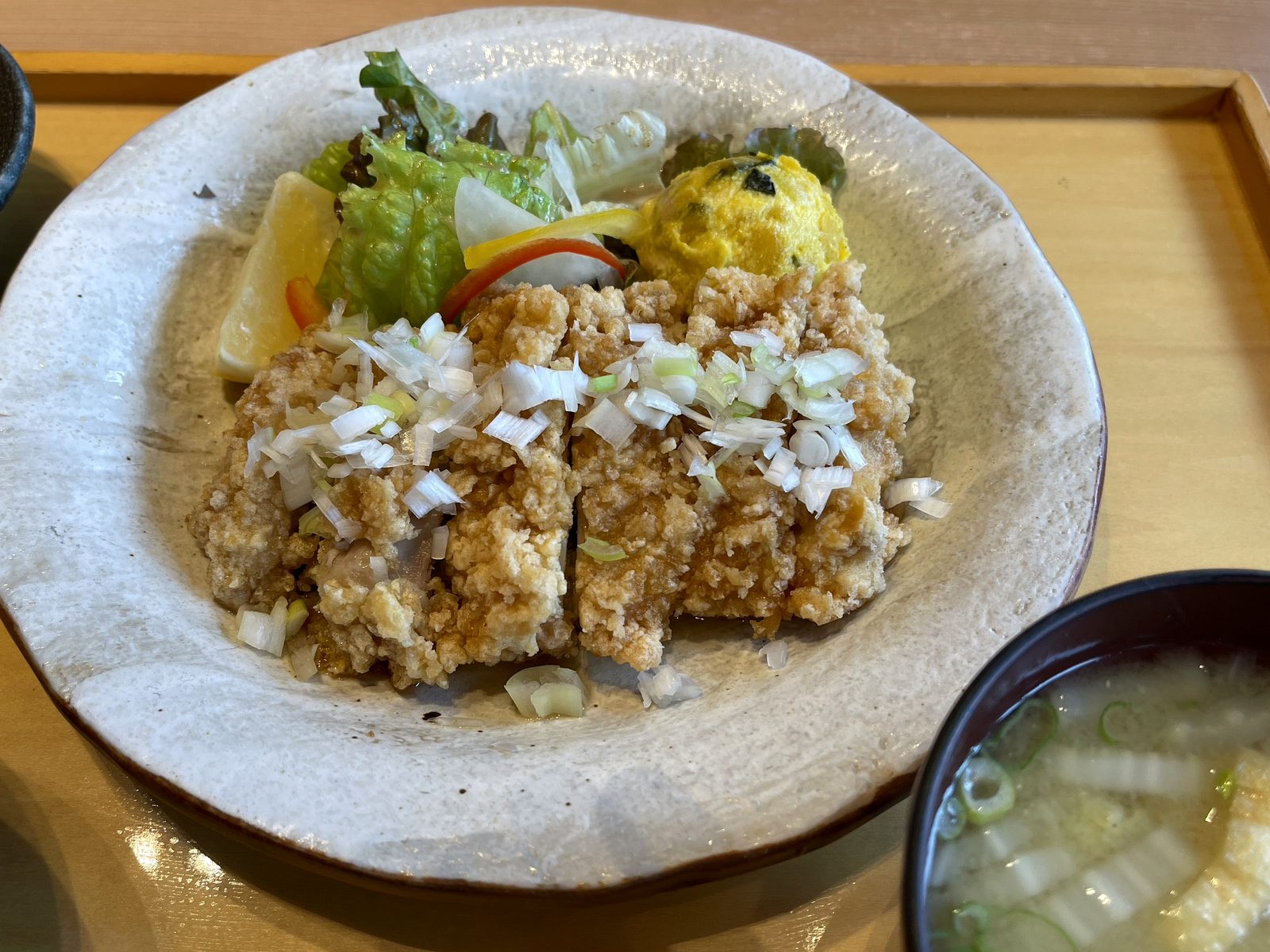 揚げ鶏の香味だれのクローズアップ。刻みネギがたっぷりのった、衣がザクッとした揚げ鶏と瀬戸内レモン