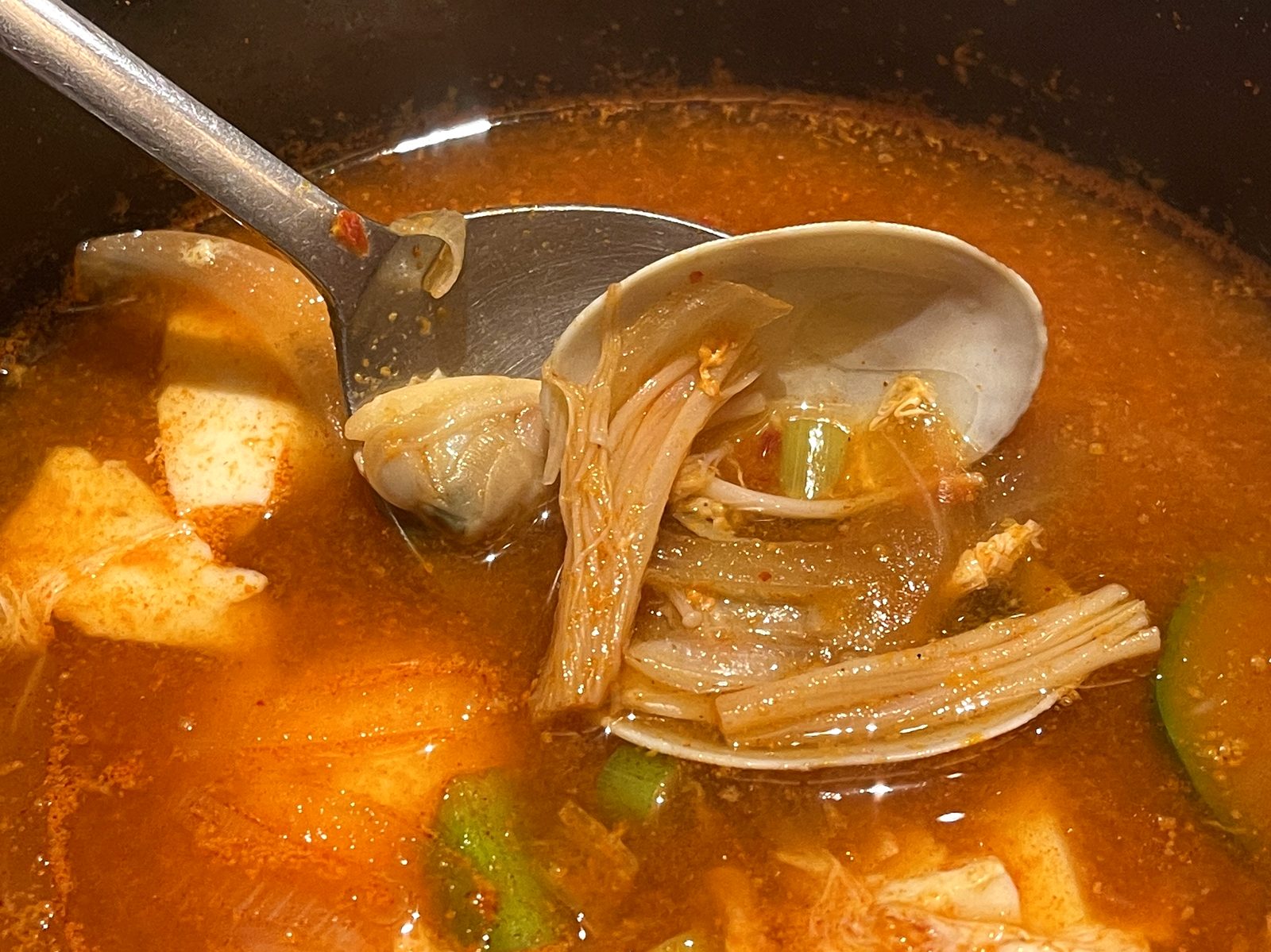 レンゲですくったスンドゥブ。殻付きのあさりとえのきが見える
