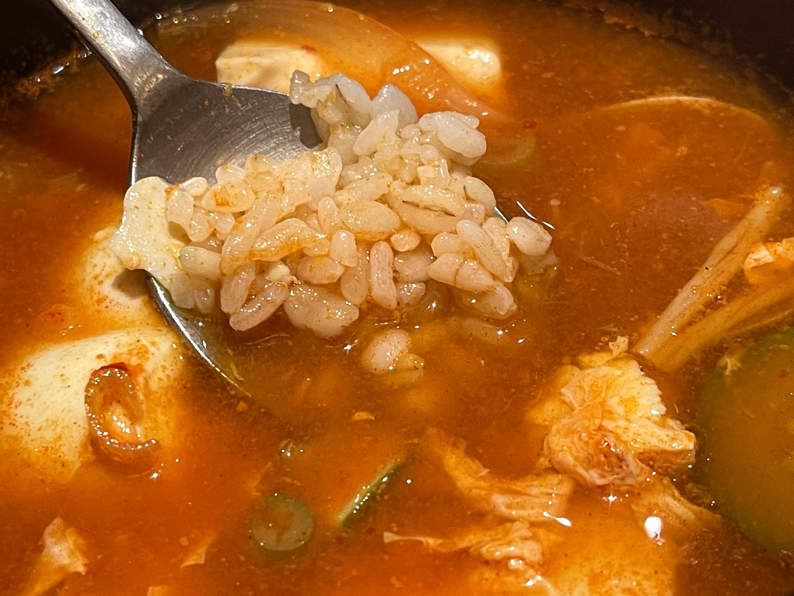 麦ご飯をスンドゥブのスープに浸したレンゲ。米粒がスープを吸っている