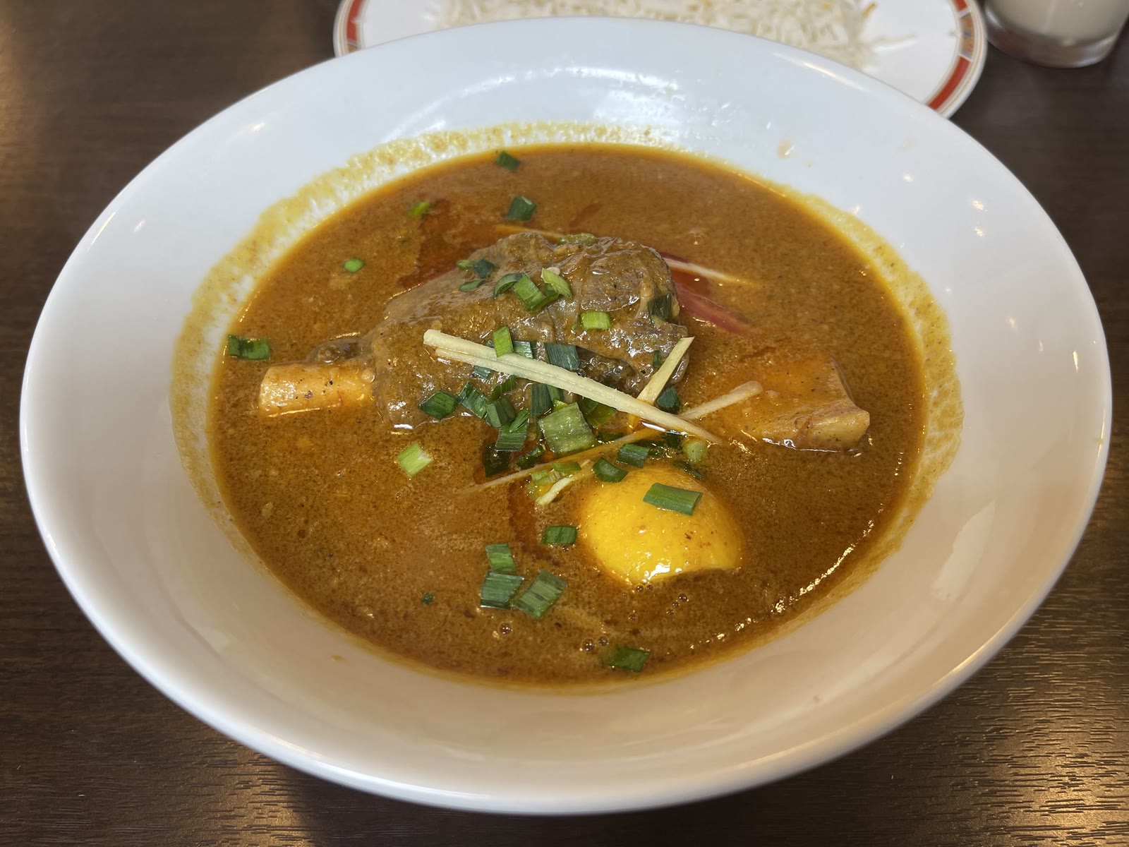 オレンジ色のニハリのスープに、骨付きの牛肉、刻み生姜、ネギ、黄色いじゃがいもが入った一皿のアップ