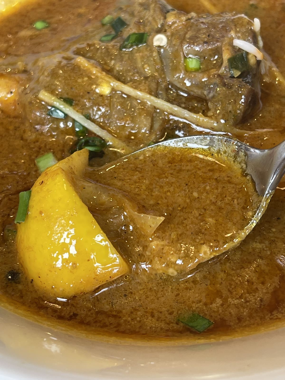 ニハリのスープをスプーンですくうアップ。黄色いじゃがいも、刻み生姜、煮込まれた牛肉が見える