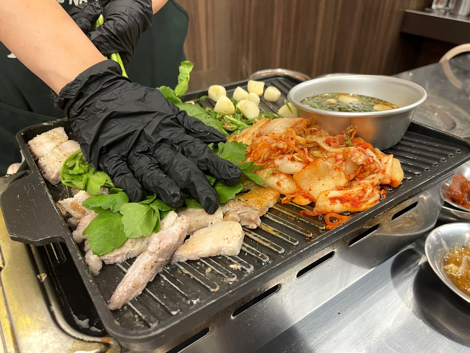 黒い手袋をしたスタッフが、鉄板の上でミナリと豚肉を整えている