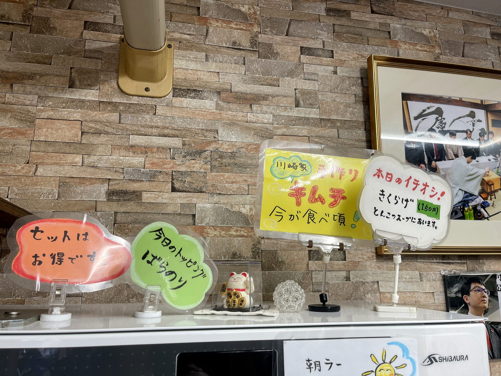 川崎家 榎町店の店内に飾られた将棋の対局写真の額と、手作りキムチ・きくらげのポップ