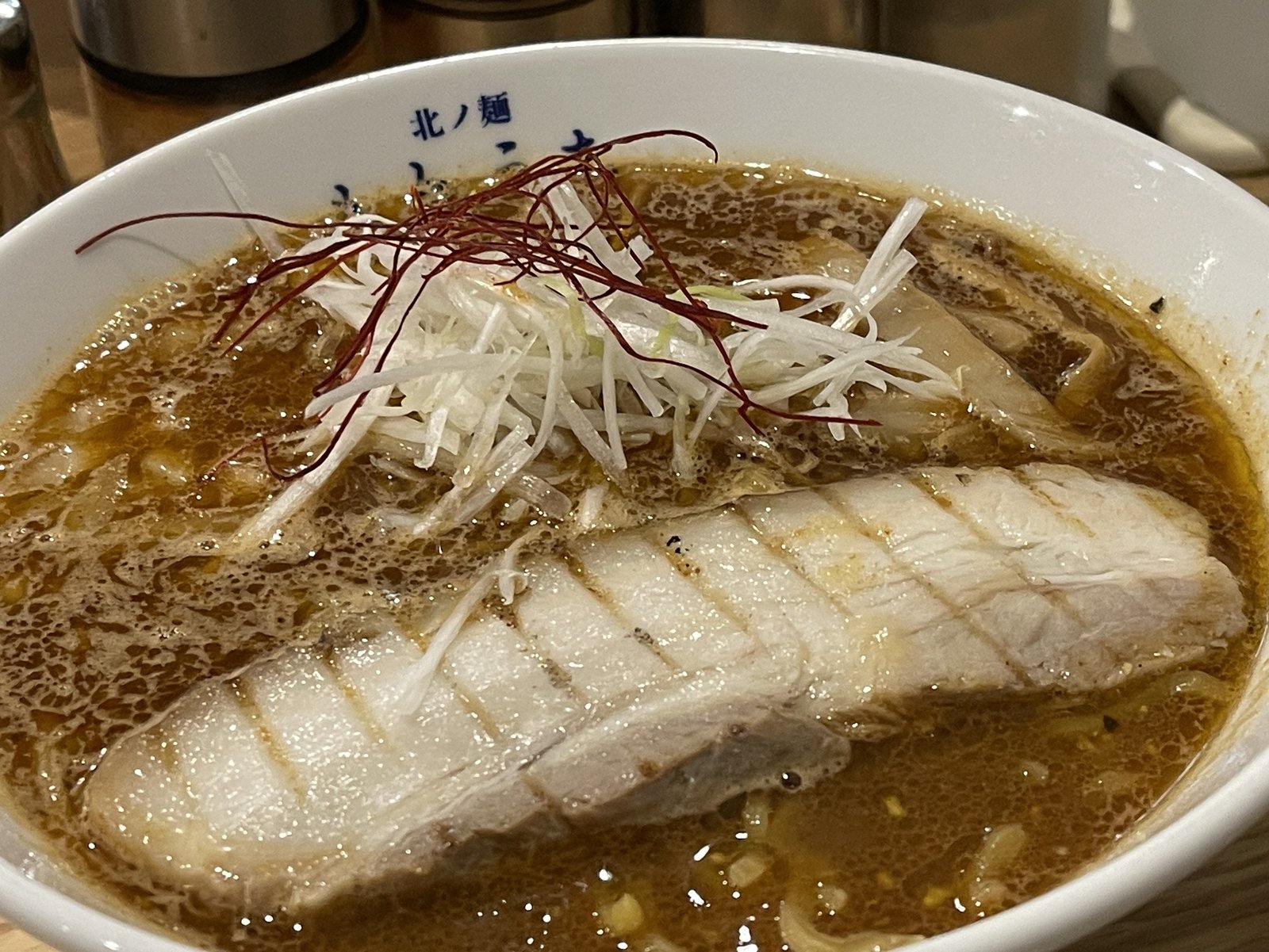 札幌スパイシーラーメンのアップ、白髪ねぎと糸唐辛子の下にバラチャーシューとメンマが見える
