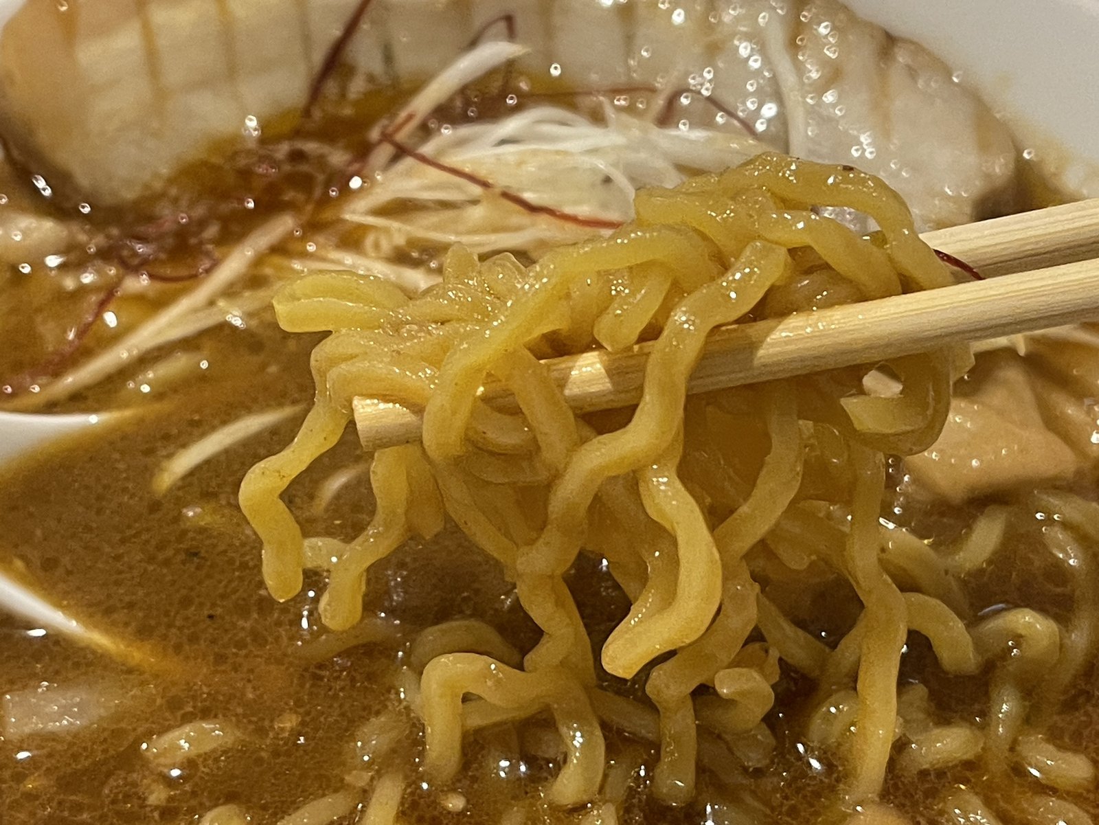 箸で持ち上げた縮れ麺のアップ、スープがよく絡んでいる様子