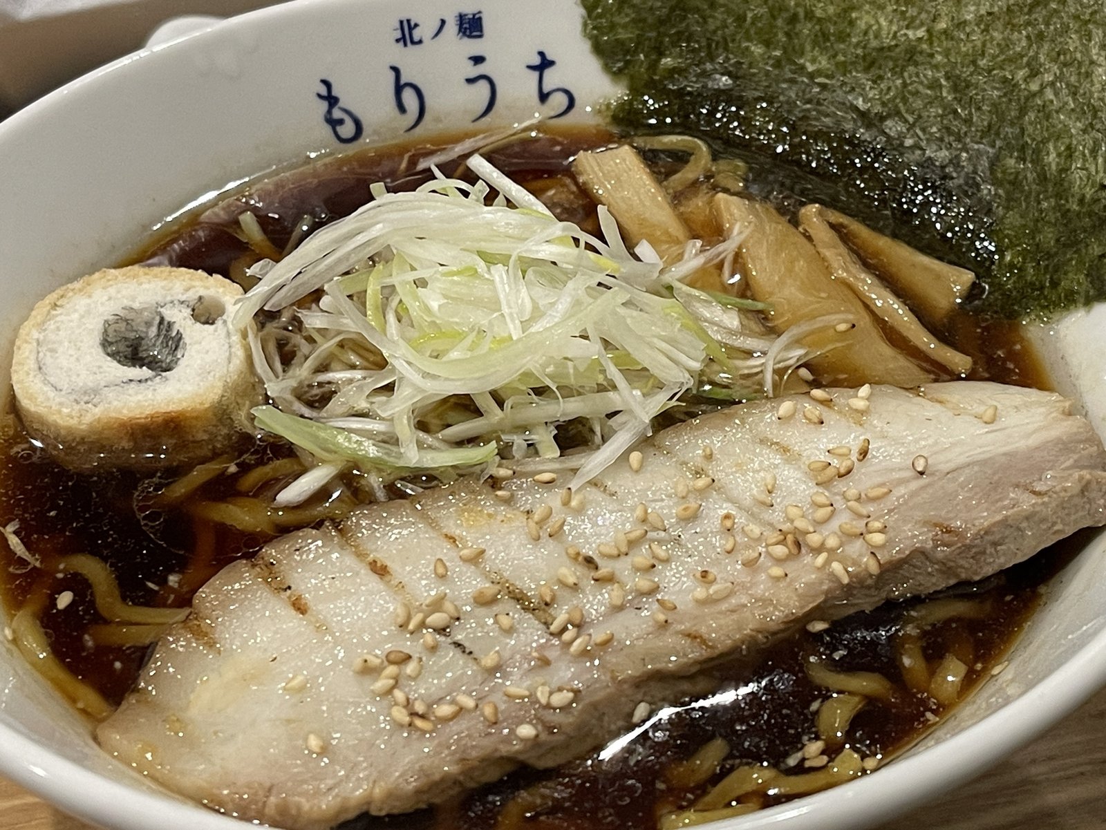 黒醤油ラーメンのアップ、白髪ねぎとメンマ、海苔、バラチャーシューがスープにのっている様子