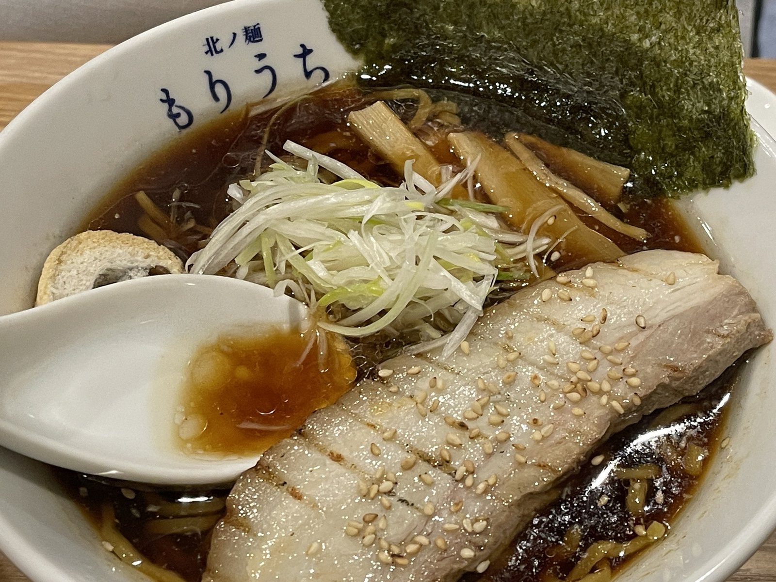れんげに黒醤油ラーメンのスープをすくったところ、茶色く濃い色のスープが見える