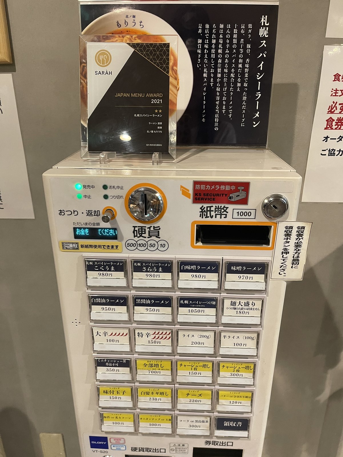 食券機の上に貼られた札幌スパイシーラーメンの説明書き、鶏ガラ・豚骨・香味野菜のだしに十数種類のスパイスを配合していると紹介されている