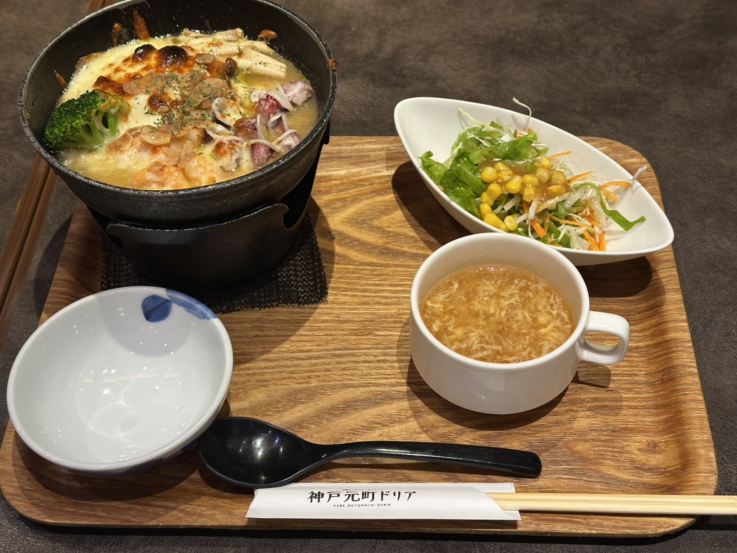 固形燃料の火にかけられた黒い鍋でグツグツと煮えるシーフードのドリア。表面のチーズにこんがり焦げ目、手前にコーン入りサラダとかきたま風スープの付いたランチセット