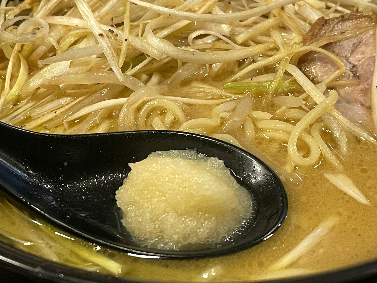 れんげに山盛りに乗せたすりおろしニンニク。ラーメンのスープに入れる直前のクローズアップ