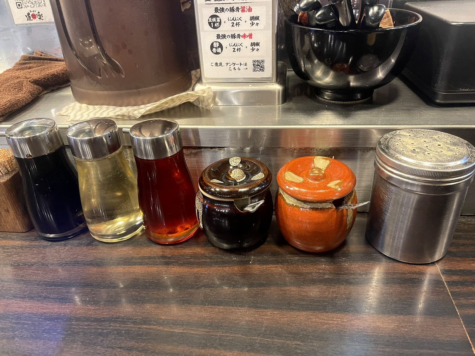 ラーメン道楽の卓上調味料一式。醤油・酢・辣油・にんにく壺・味噌壺・胡椒挽きが並ぶ