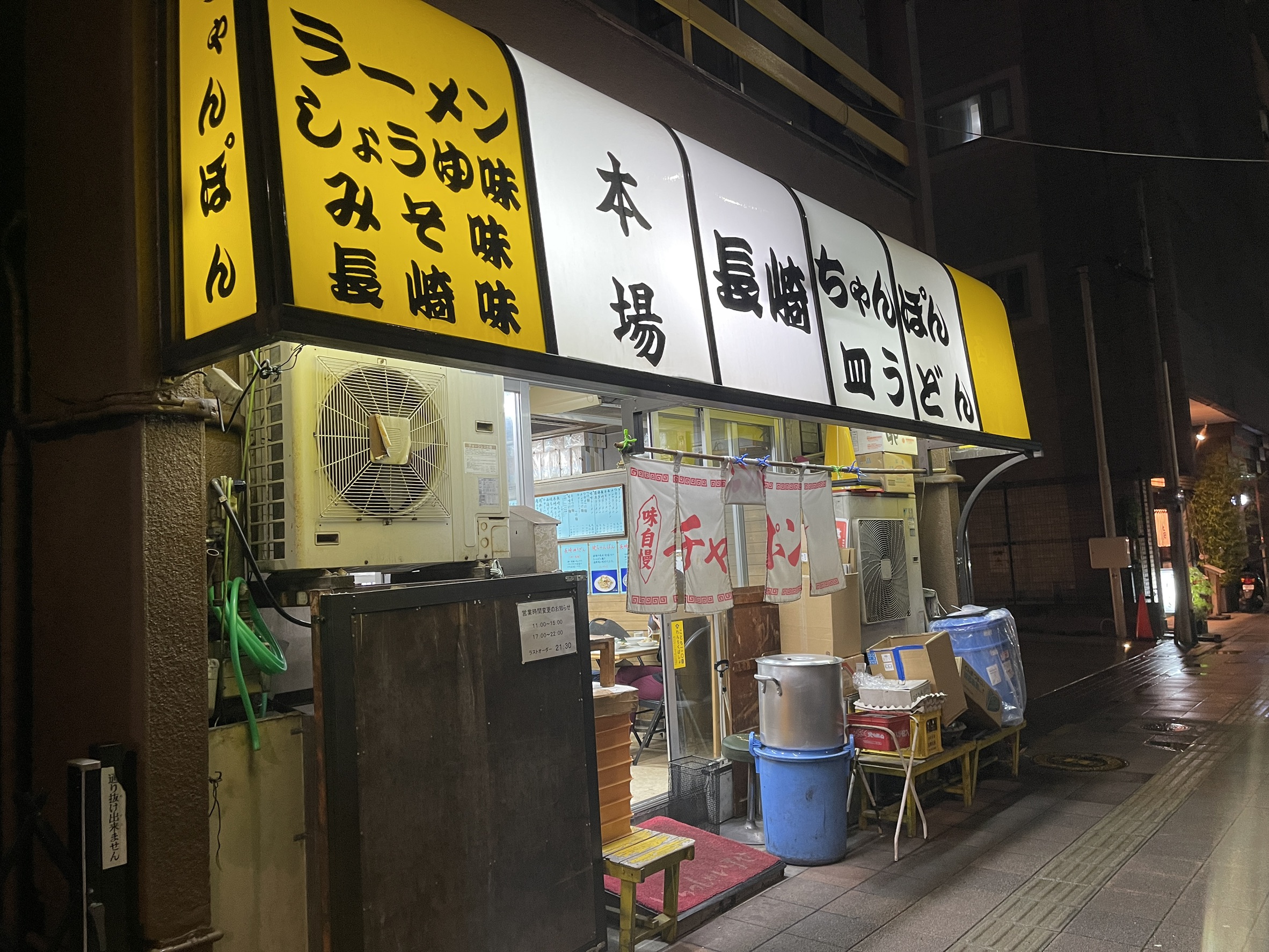 夜の西海の外観。黄色い電飾看板に「本場 長崎ちゃんぽん 皿うどん」「ラーメン しょうゆ味 みそ味 長崎味」と書かれ、赤いのれんが下がる街の中華店