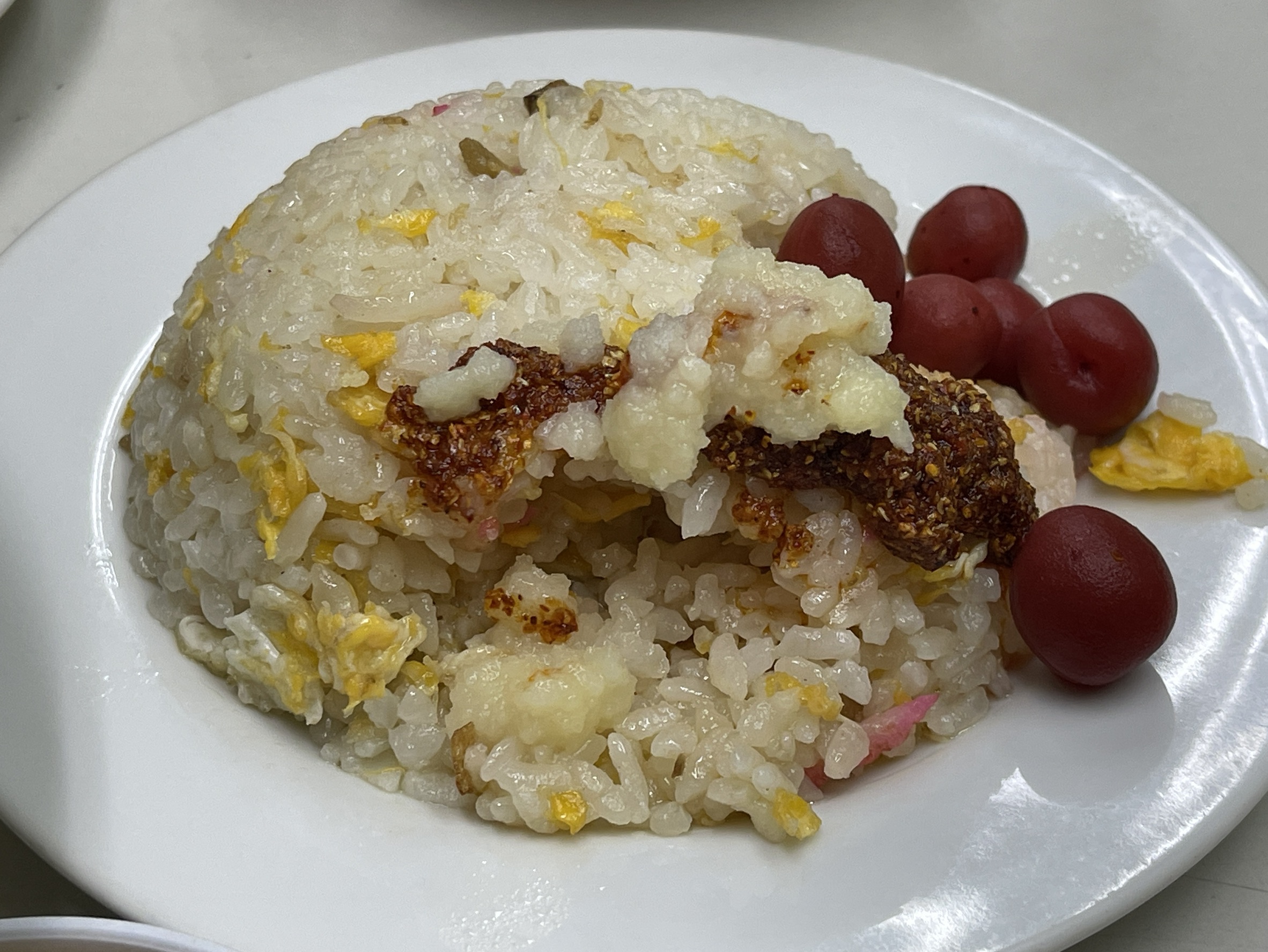 半チャーハンのアップ。卵とかまぼこが混ざったチャーハンの上に、おろしにんにくと粒ラー油がのり、脇に赤いカリカリ梅が添えられている