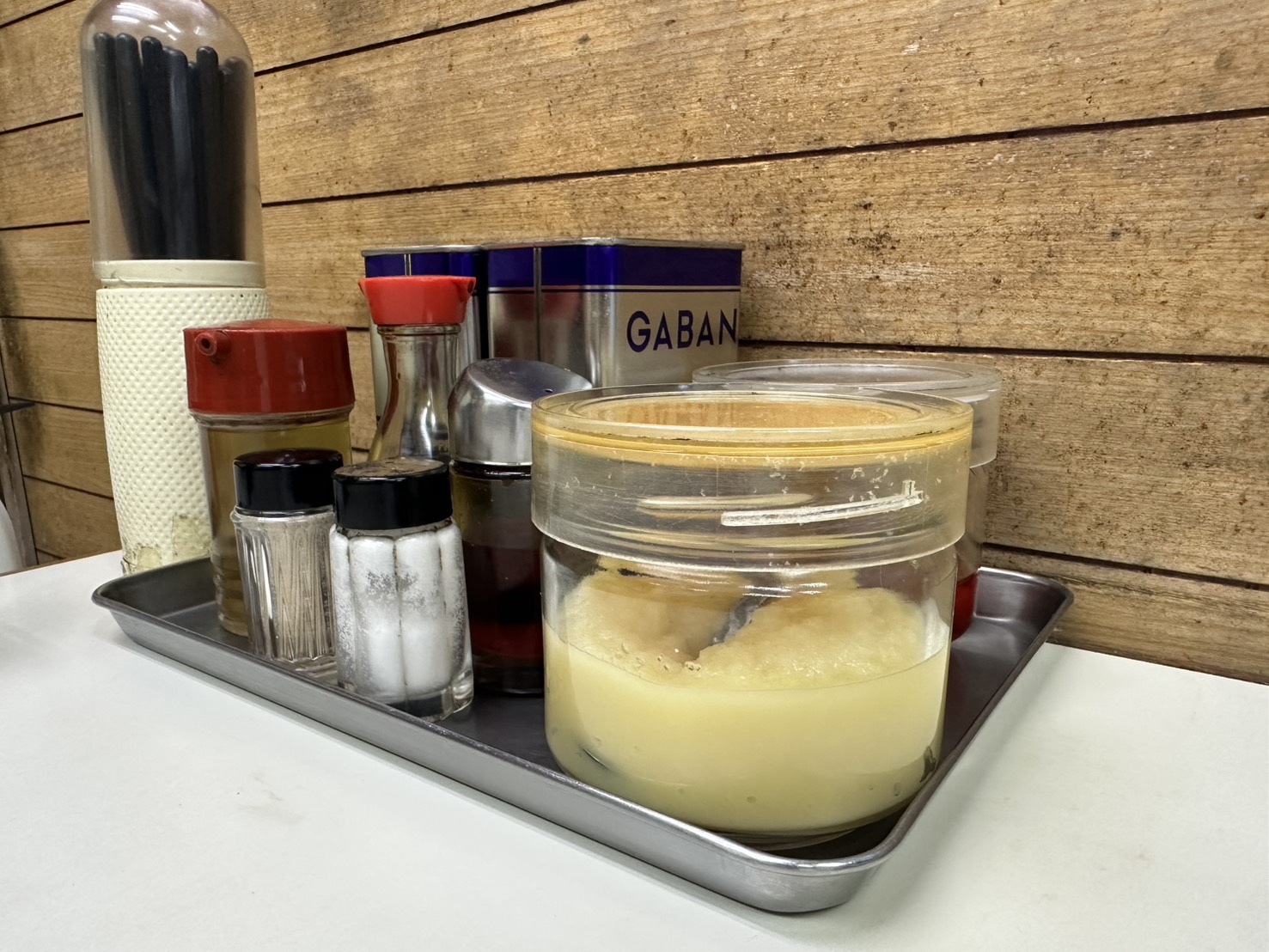卓上の調味料トレイ。白胡椒(GABAN)、ラー油、塩、醤油さし、おろしにんにくの入った容器が並ぶ