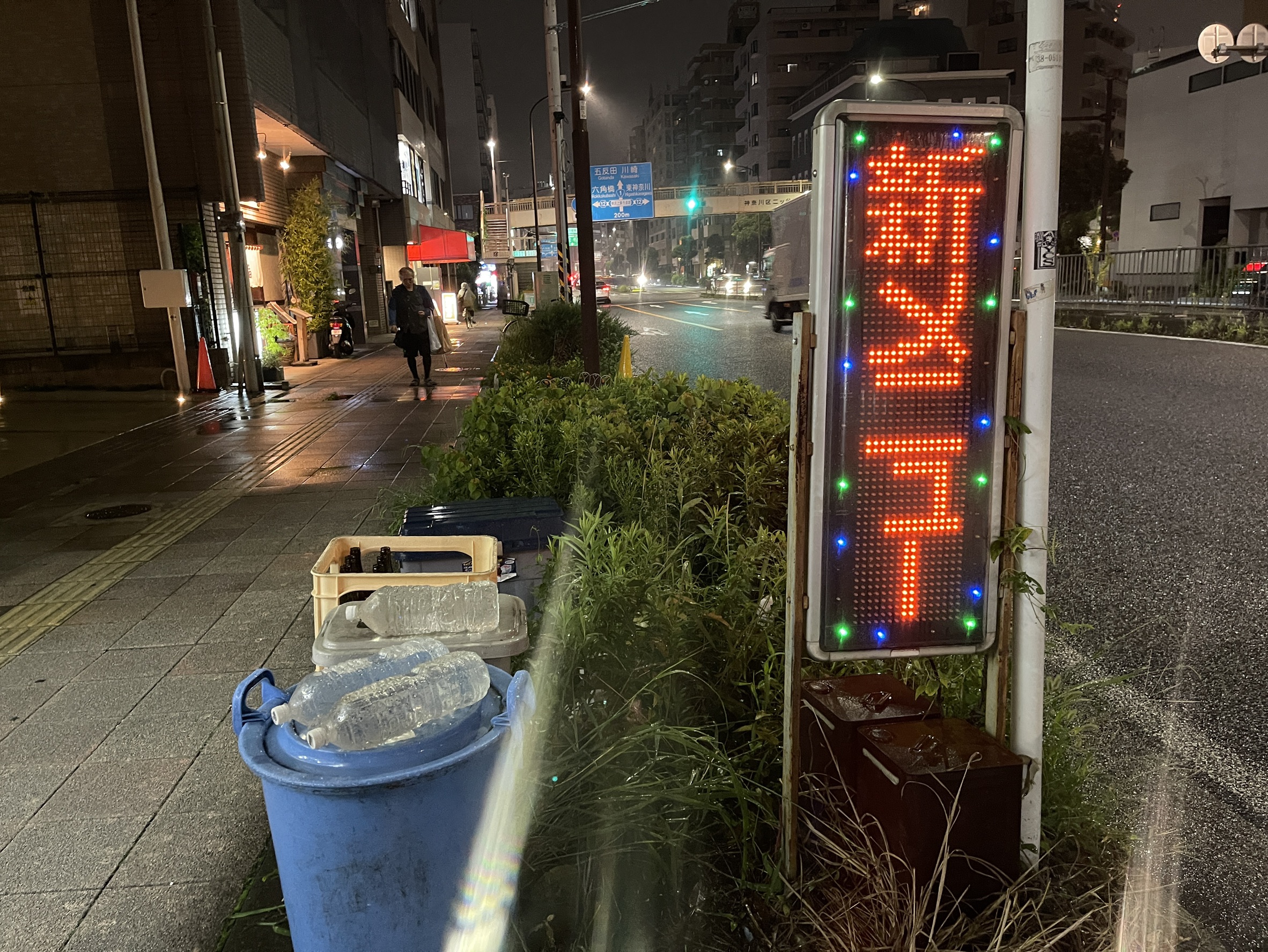 夜の通り沿いの様子。赤いLED表示の看板と、五反田・川崎・東神奈川方面を示す道路標識が見える横浜市神奈川区の街並み