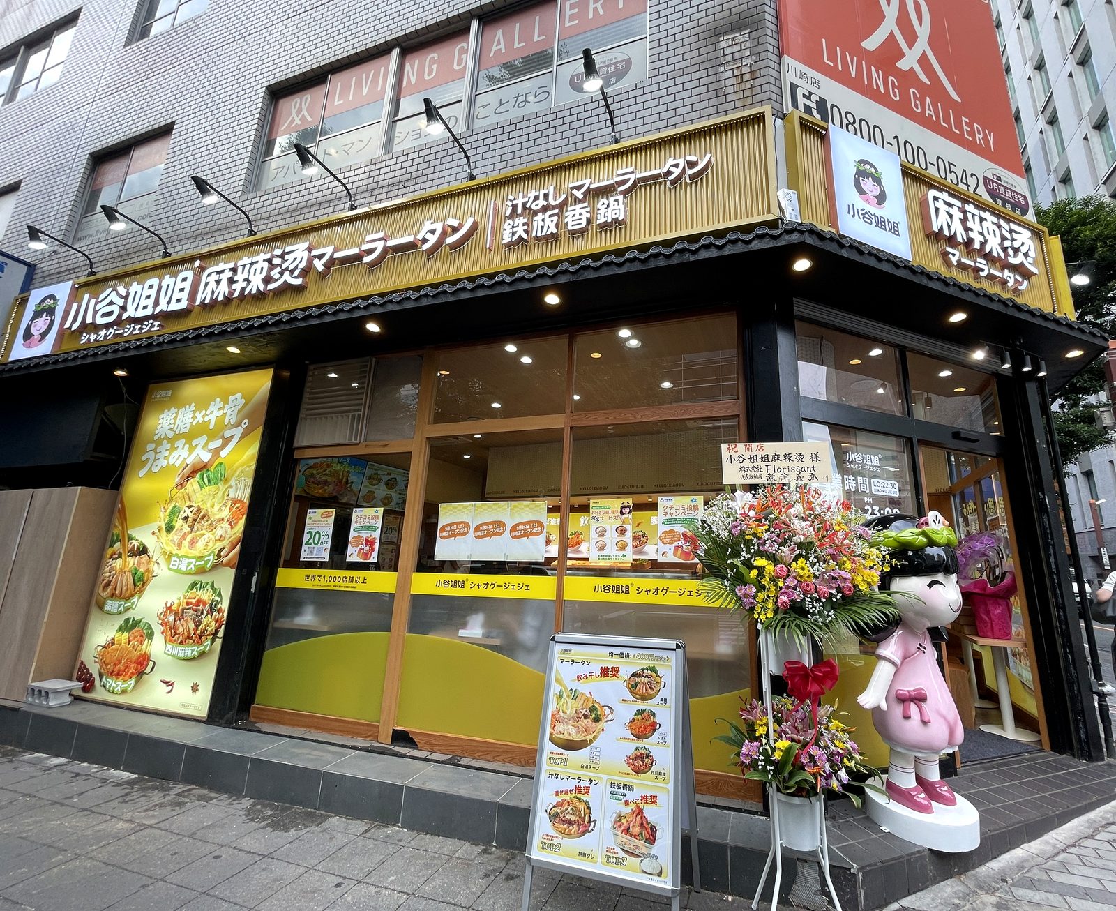 小谷姐姐 川崎店の外観。開店祝いの花スタンドとピンクのキャラクター人形、店頭に9/26オープンや20%OFFのポスターが並ぶ