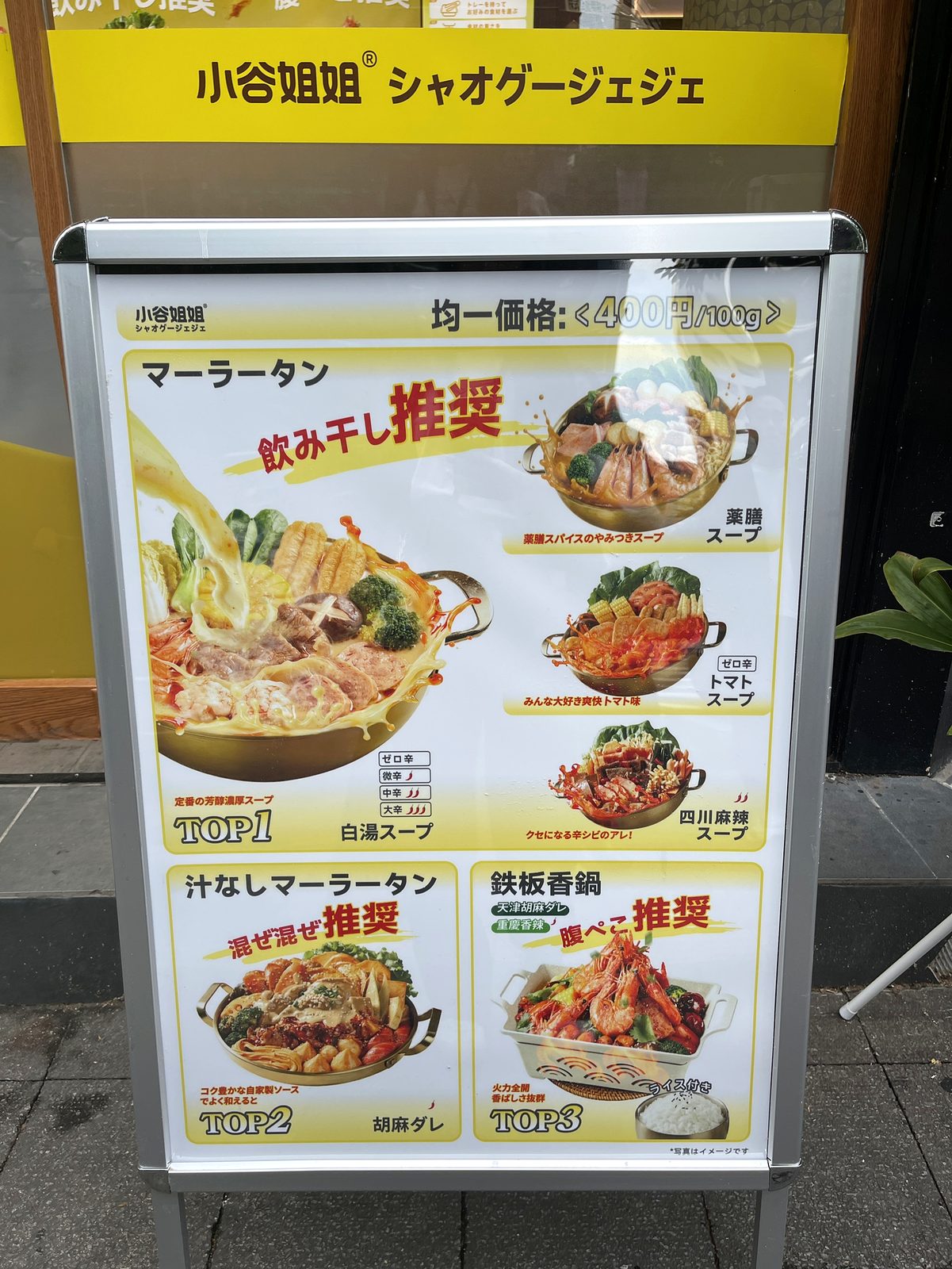 小谷姐姐 川崎店 店頭のA看板メニュー。均一価格400円/100g、白湯・薬膳・トマト・四川麻辣の4スープ、汁なしマーラータン、鉄板香鍋が写真つきで一覧できる