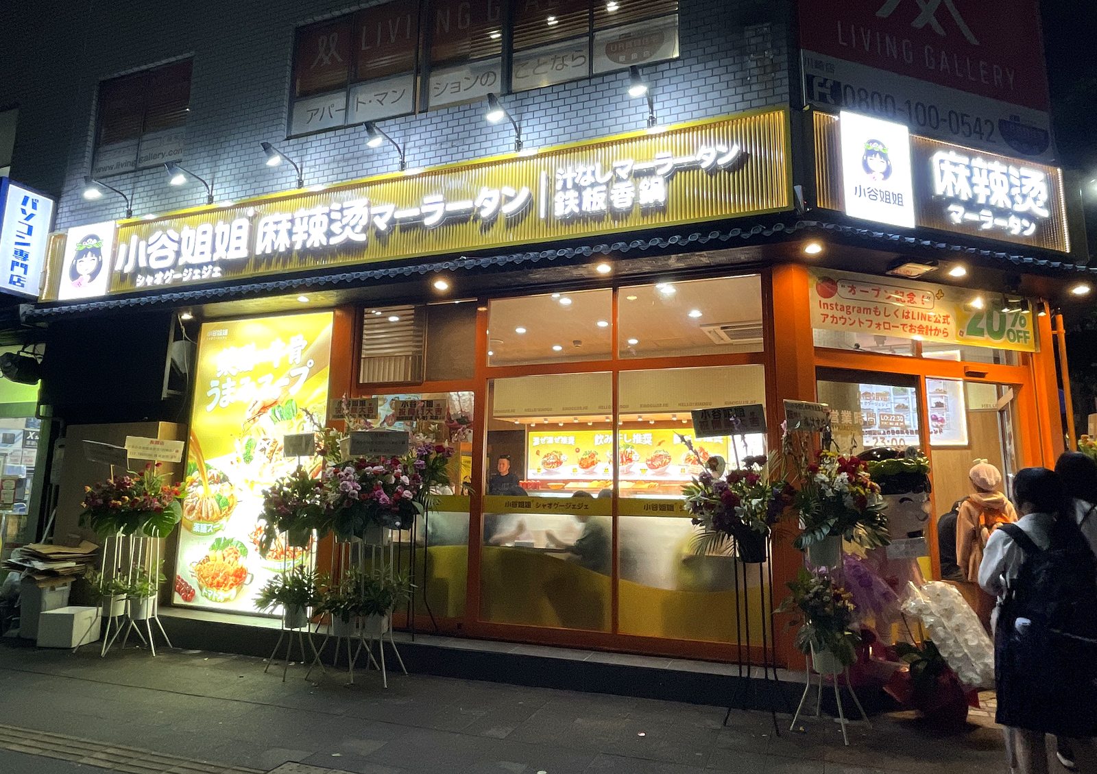 夜に訪れた小谷姐姐 川崎店の外観。開店祝いの花スタンドやオープン記念の案内が並ぶ