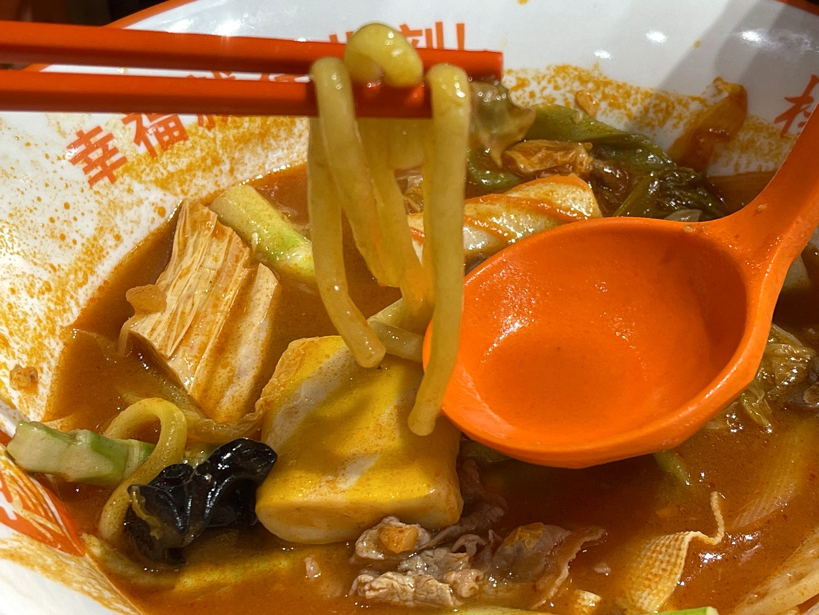 黄色くて太めの牛すじ麺をお箸で持ち上げているところ