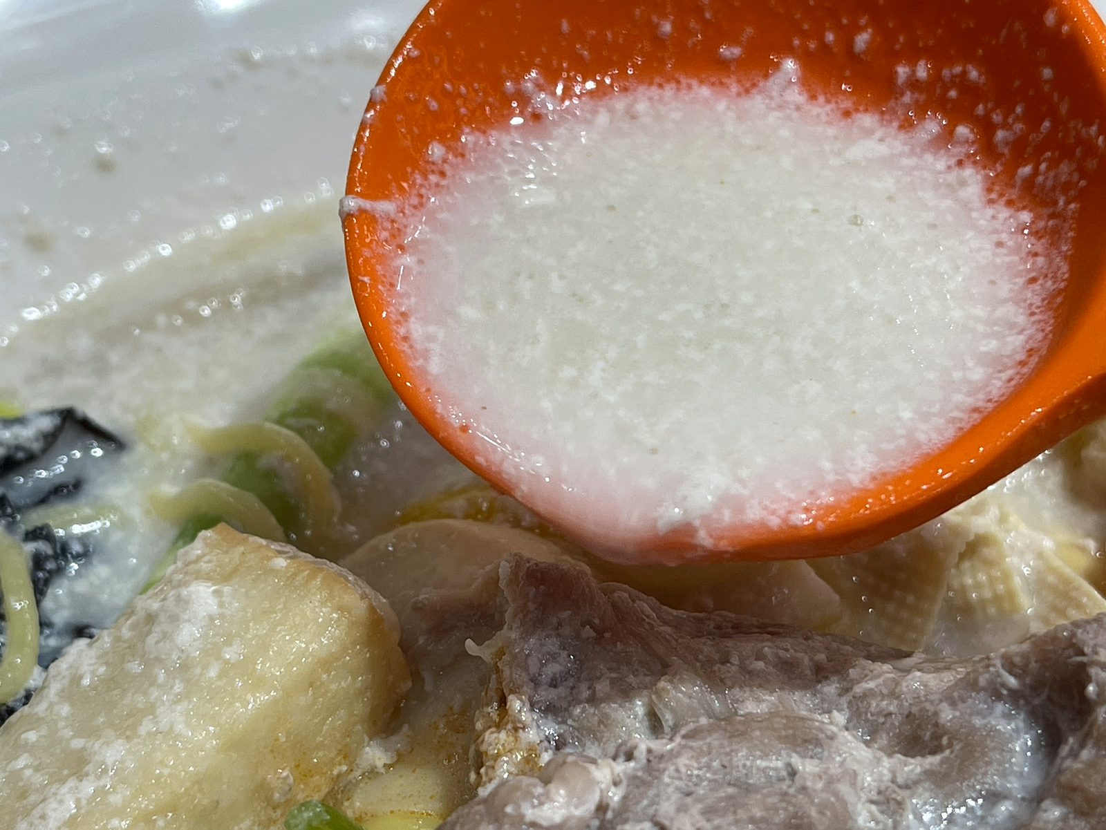 オレンジのレンゲですくった白くとろみのある牛骨スープ