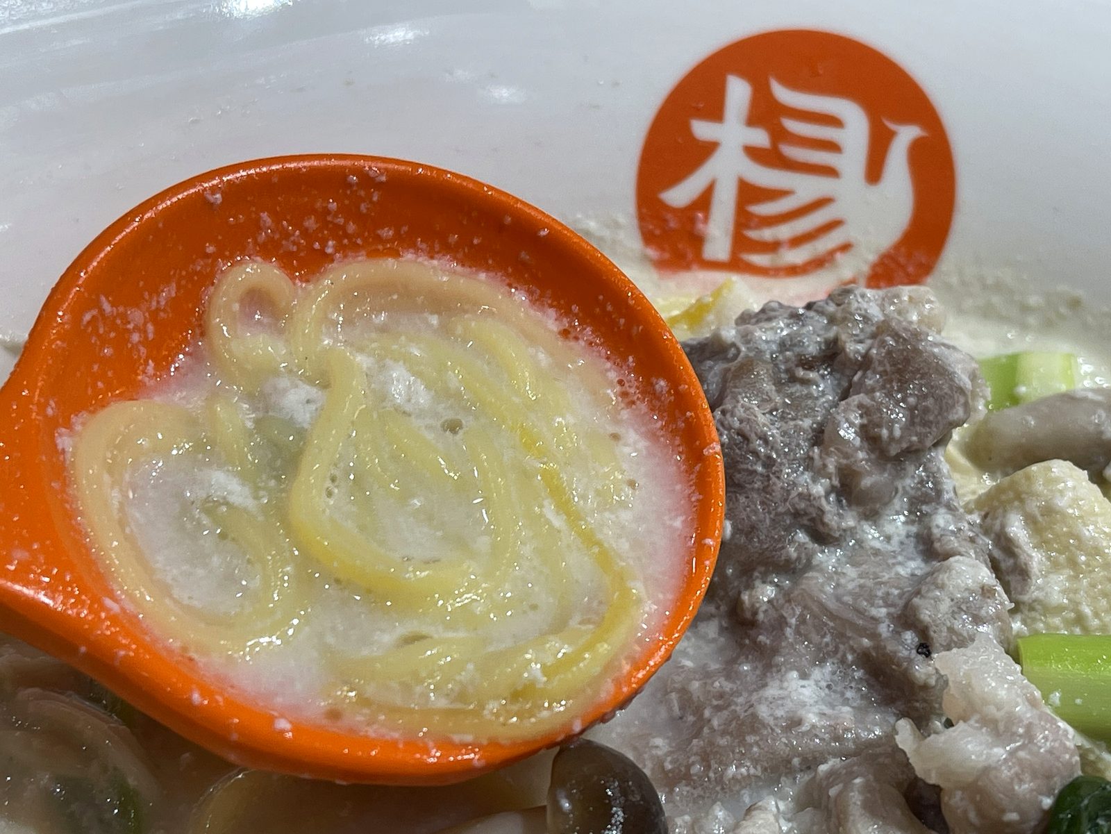 黄色い渦巻き状のとうもろこし麺をオレンジのレンゲに乗せたクローズアップ