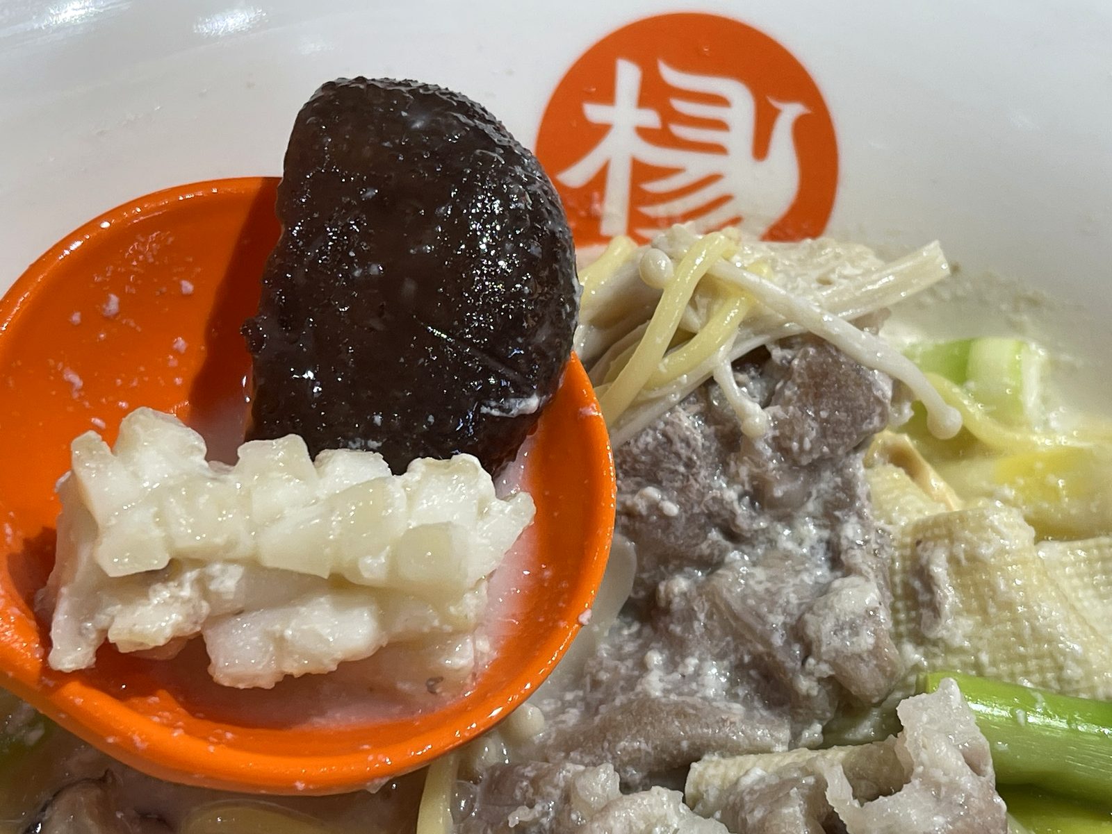 切れ込みの入ったイカと黒いキクラゲをレンゲに乗せたクローズアップ