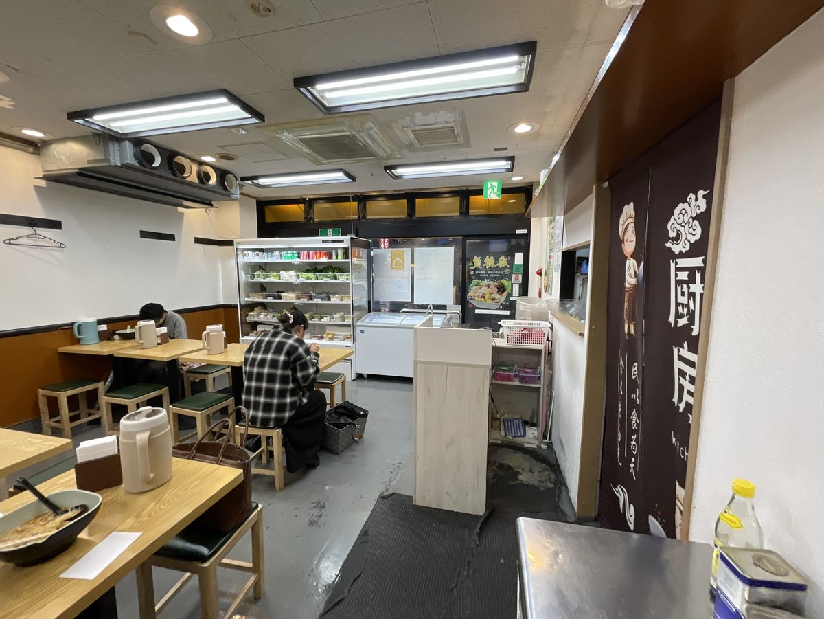 テーブル席とドリンクの冷蔵庫厨房の暖簾が見える三寅馬重慶麻辣燙の店内