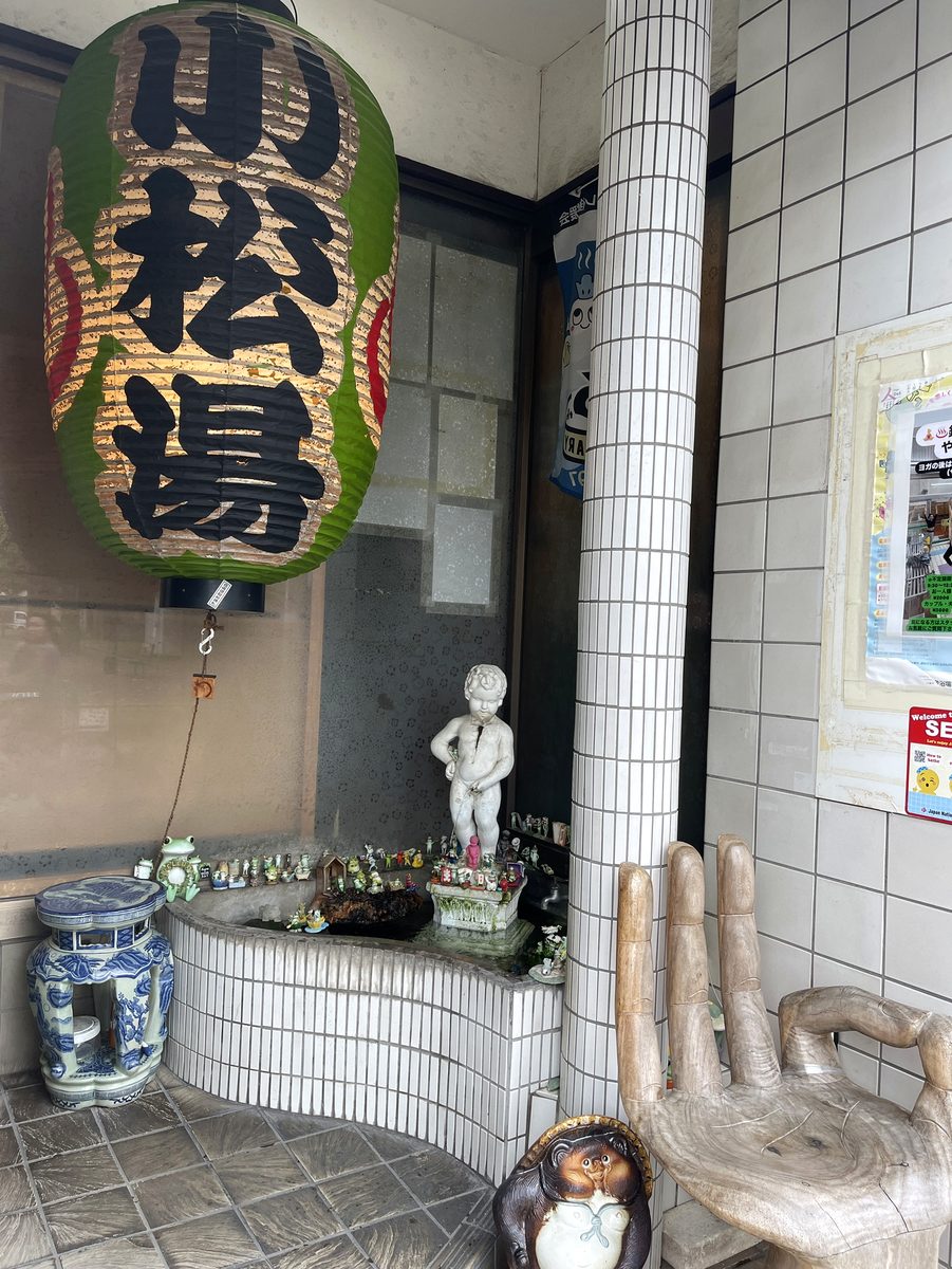 巨大な緑の「小松湯」提灯と、フィギュアがびっしり並ぶ入口の置物